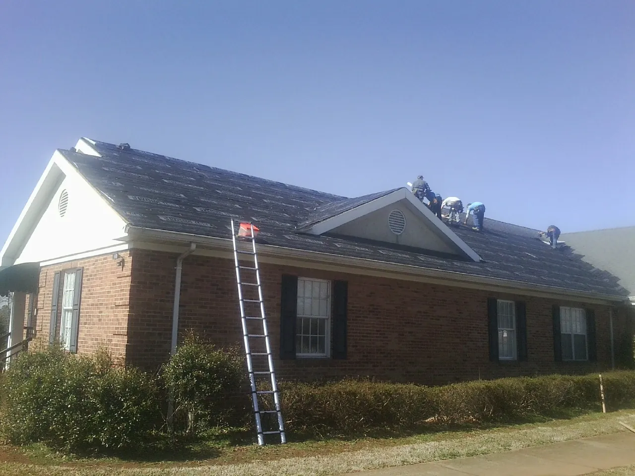 Crew tearing shingles off a brick ranch roof with a ladder set — Emergency Roof Repair work by our crew in La Canada Flintridge