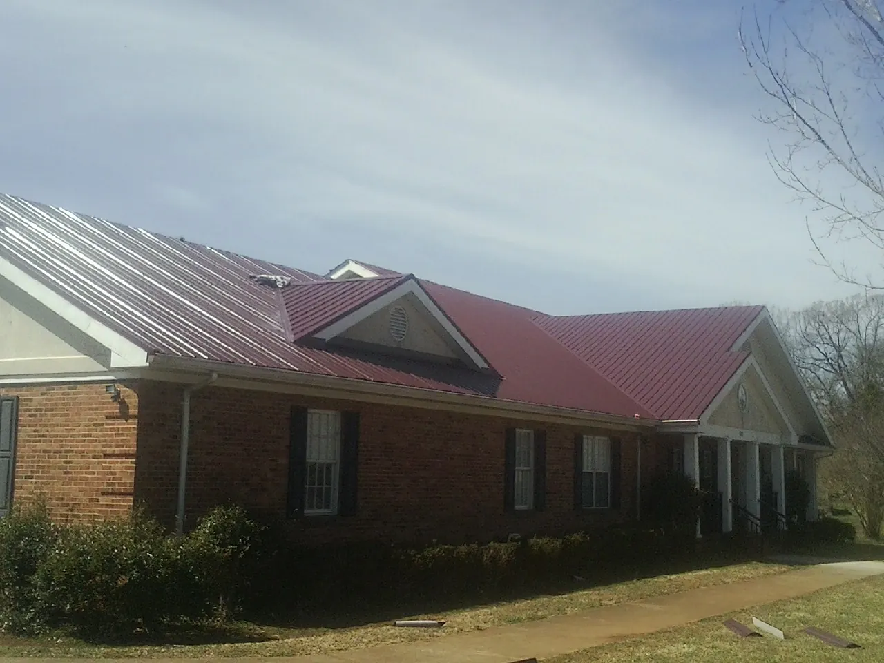 Red metal roof with gabled entries on a long brick building, from a Hail Damage Roof Repair job in La Canada Flintridge