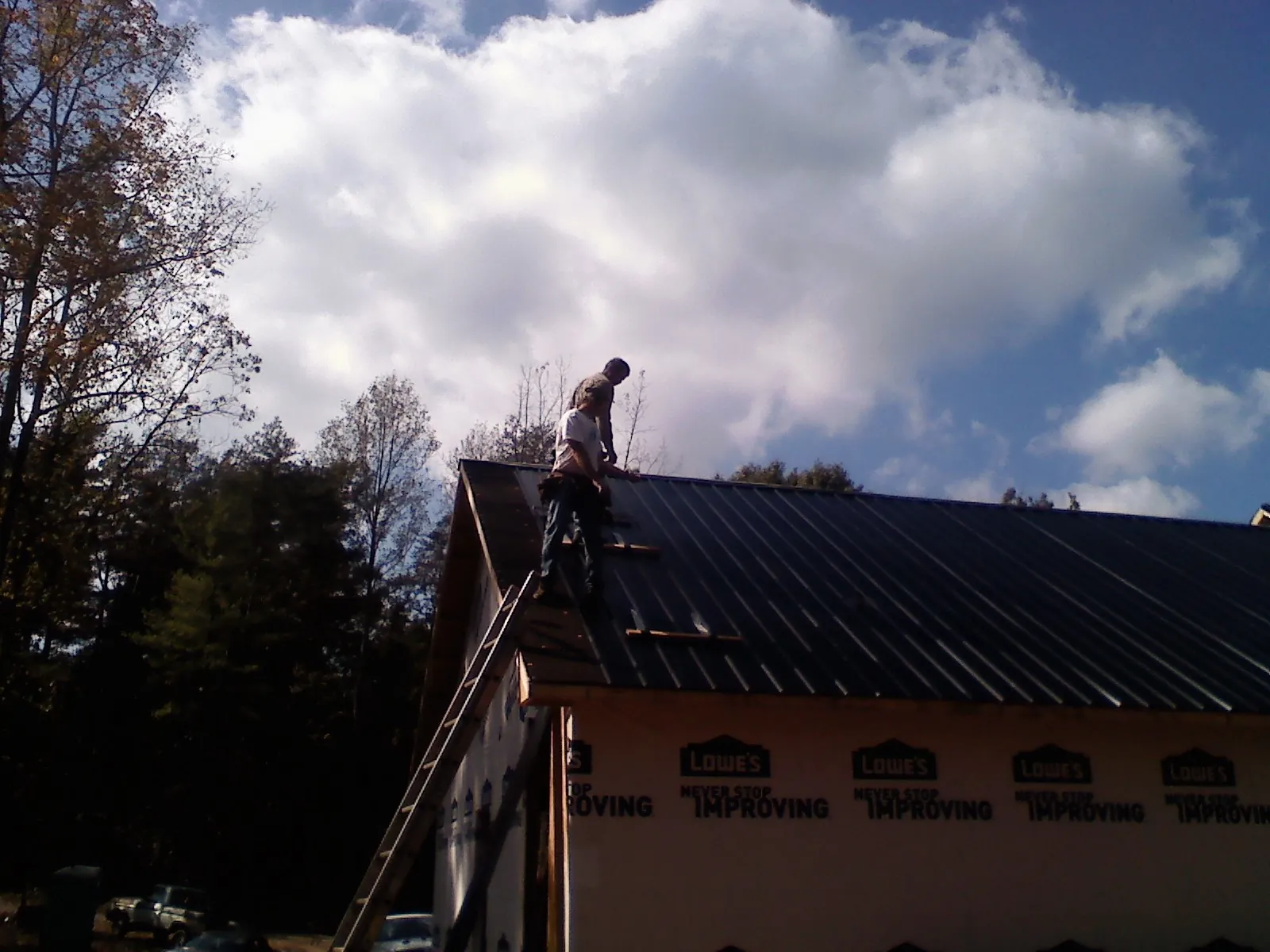 Roofer fastening dark metal panels high against a cloudy sky, from a Roof Inspection job in La Canada Flintridge